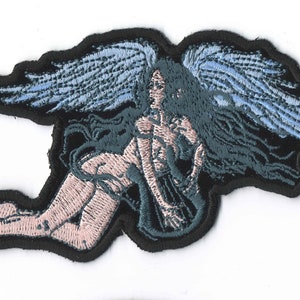 May include: Embroidered patch featuring a nude woman with wings, lying on her side with her head turned to the side. The wings are blue and the woman's hair is black. The patch is on a black background.