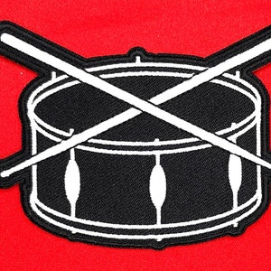 May include: Black and white embroidered patch of a drum with two drumsticks crossed over the top.