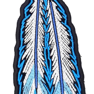 May include: A blue and white embroidered patch of two feathers with a dreamcatcher at the top. The dreamcatcher is brown and has a blue circle around it.