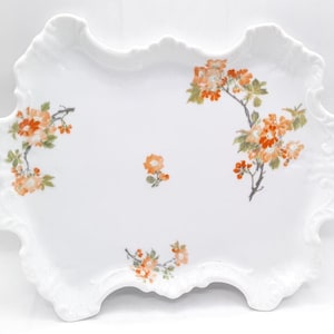 May include: A white porcelain serving tray with a scalloped edge and a floral design featuring orange and green flowers.