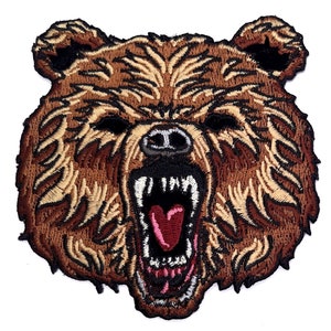May include: Embroidered patch of a brown bear's face with a fierce expression, its mouth open in a growl, showing sharp teeth and a pink tongue.