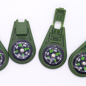May include: Four green compass keychains with a black compass face and green lettering. The compass face has the letters N, S, E, and W, and the directions are marked in between.