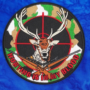 May include: Embroidered patch featuring a deer with large antlers, a red crosshair, and two crossed rifles. The patch has a camouflage border and the text "HUNTING IS IN MY BLOOD" in red.