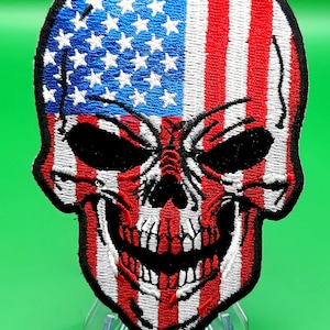 May include: An embroidered patch featuring a skull with the American flag design. The skull is white with black eyes and a black mouth. The flag is red, white, and blue.