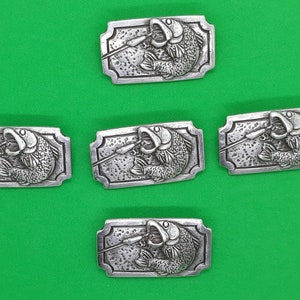May include: Five silver-toned metal belt buckles with a detailed design of a fish being caught on a fishing line. The buckles are rectangular and have a slightly ornate border.