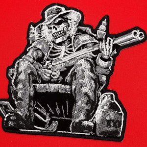 May include: Embroidered iron-on patch featuring a skeleton wearing a cowboy hat and holding a gun. The skeleton is sitting in a chair with a bottle on the ground next to it.