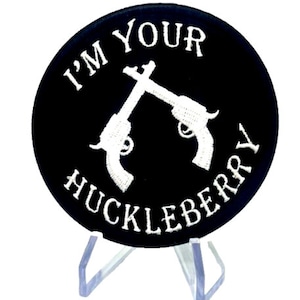 May include: A black embroidered patch with white stitching. The patch is round and features two crossed pistols with the text "I'm Your Huckleberry" around the pistols.