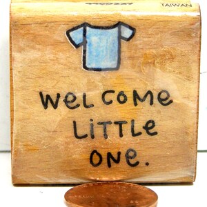 May include: Wooden stamp with a blue t-shirt graphic and the text "Welcome Little One."