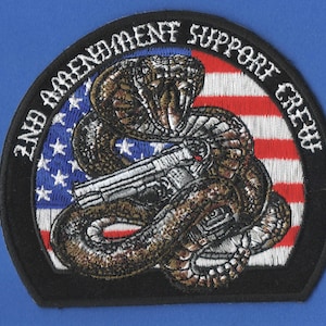 May include: Embroidered patch with a black background, featuring a coiled cobra with a handgun in its mouth, against a red, white, and blue American flag. The text "2nd Amendment Support Crew" is written in a white circular border around the image.