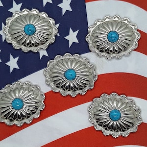 May include: Five silver-colored conchos with a turquoise-colored center stone. The conchos are oval-shaped with a scalloped edge and a sunburst design. The background is the American flag.