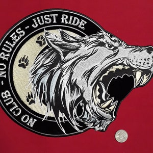 May include: Black and white embroidered patch with a snarling wolf head in the center. The wolf's mouth is open and its teeth are visible. The patch is surrounded by a black circle with the text "NO CLUB - NO RULES - JUST RIDE" in white.