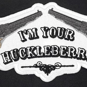 May include: White embroidered patch with two pistols crossed behind the text "I'm Your Huckleberry".