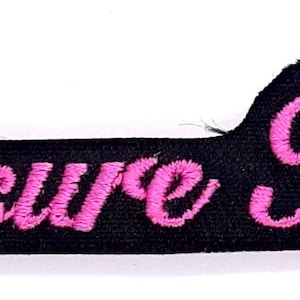 May include: Black fabric patch with pink embroidered text that reads "Pleasure Kitten".