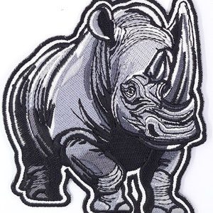 May include: A black and white embroidered patch of a rhinoceros. The rhinoceros is standing with its legs spread apart and its head tilted slightly to the side. The patch is detailed and realistic.