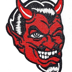 May include: Red devil head with horns, a single eye, and a mischievous grin. The devil is winking and has a black and white outline.