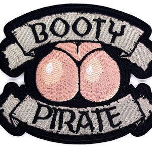 May include: Embroidered patch with the words "BOOTY PIRATE" in gray lettering on a gray banner. The patch features a pink and white illustration of a rear end. The patch has a black border.