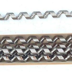 May include: A set of silver-colored auger drill bits, one displayed separately and the others in a cardboard box. The drill bits have a spiral design and a pointed tip. The box contains four additional drill bits. The drill bits are for woodworking or construction.