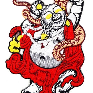 May include: Embroidered iron-on patch featuring a smiling, white, cartoon-style Buddha figure wearing a red robe and holding a golden orb. The Buddha is surrounded by swirling, orange and brown, embroidered details.