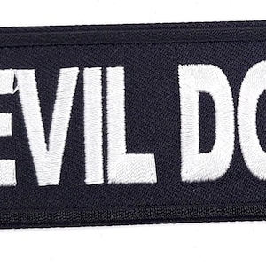 May include: Black embroidered patch with white text that reads "DEVIL DOG".