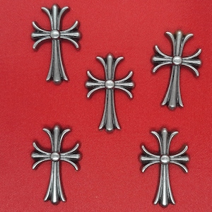 May include: Five silver-toned cross charms with a detailed design. The crosses have a rounded center and are slightly raised from the surface.