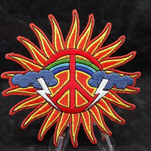 May include: A red, yellow, and blue embroidered patch featuring a peace sign with a rainbow and lightning bolts in a sunburst design.