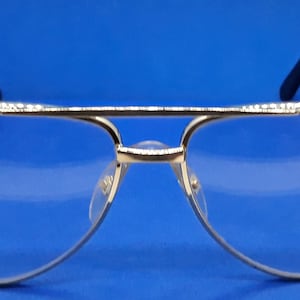 May include: Gold-rimmed aviator style safety glasses with clear lenses and clear plastic side shields.