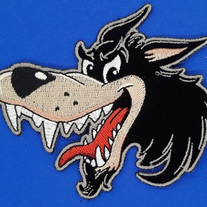 May include: A black and white embroidered patch of a cartoon wolf with a red tongue sticking out. The wolf has a menacing expression with sharp teeth and a furrowed brow.