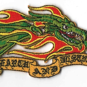 May include: Embroidered patch featuring a green dragon with red and yellow flames. The dragon holds a gray object in its claw. A banner below reads "MARCH AND DISMAY" in gold lettering. The patch is likely for clothing or accessories.