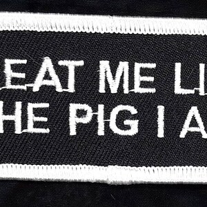 May include: Black and white embroidered patch with white stitching around the edges. The patch reads "Treat me like the pig I am."