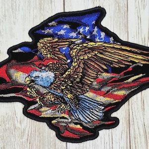 May include: Embroidered patch featuring a detailed bald eagle with outstretched wings, set against a backdrop of the American flag. The patch has a black border and showcases red, white, blue, and brown colors.