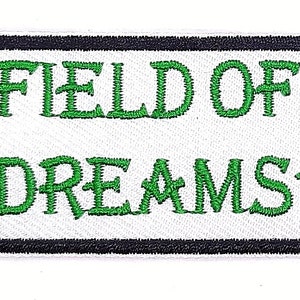 May include: White rectangular patch with black border and green embroidered marijuana leaves on either side of the text "FIELD OF DREAMS".