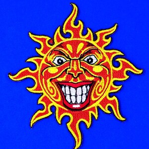 May include: Embroidered patch featuring a grinning sun with a fiery, red and yellow design. The sun has a wide, toothy grin and a detailed face. The patch is set against a vibrant blue background, suitable for jackets or bags.