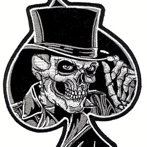 May include: Black and white embroidered patch of a skull wearing a top hat and a jacket, in the shape of a spade playing card.