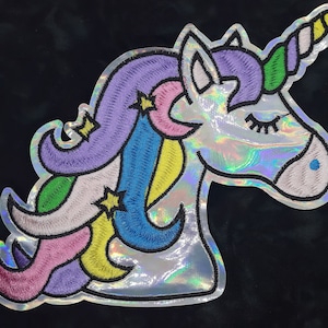 May include: A silver iridescent unicorn head with a rainbow mane and horn. The unicorn has a closed eye and a light blue nose.