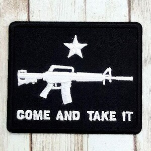 May include: Black rectangular patch featuring a white rifle, a star, and the text "COME AND TAKE IT." The patch has a black border and is likely made of fabric. The design is a bold, patriotic statement.