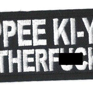 May include: Black patch with white embroidered text that reads "Yippee Ki-Yay Motherf***er".