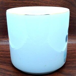 K&ouml;nnte beinhalten: Eine hellblaue Keramiktasse mit goldfarbenem Rand. Die Tasse hat ein schlichtes Design mit einigen abstrakten Formen in Blau, Wei&szlig; und Schwarz.