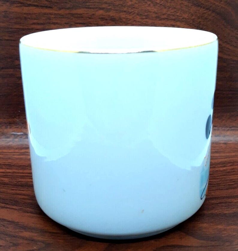 K&ouml;nnte beinhalten: Eine hellblaue Keramiktasse mit goldfarbenem Rand. Die Tasse hat ein schlichtes Design mit einigen abstrakten Formen in Blau, Wei&szlig; und Schwarz.