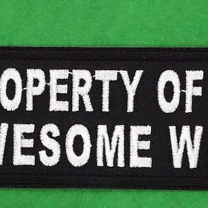 May include: Black patch with white embroidered text that reads "PROPERTY OF AN AWESOME WIFE".