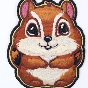 May include: Embroidered patch featuring a cartoon chipmunk with large, expressive eyes and a friendly smile. The chipmunk has brown fur with white and black accents, pink ears, and is outlined in black and yellow.
