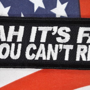May include: Black rectangular patch with white embroidered text: "YEAH IT'S FAST NO YOU CAN'T RIDE IT." The patch is set against a backdrop of an American flag, with red and white stripes and white stars on a blue field.