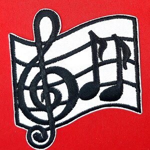May include: Black and white embroidered patch featuring a treble clef and musical notes on a white background. The patch is shaped like a flag.