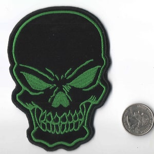 May include: Black skull patch with green embroidered details. The skull has a menacing expression with large, green eyes.