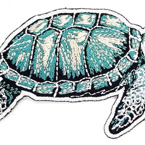 May include: Embroidered patch of a sea turtle in shades of teal, white, and black. The turtle's shell features a detailed pattern, and the patch has a black border with white stitching.