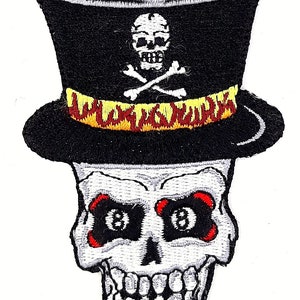 May include: Embroidered patch featuring a white skull wearing a black top hat with a yellow and red band that reads "WILD JACKS". The skull has red and black 8-ball eyes and a toothy grin.