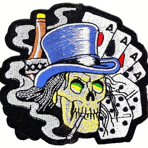 May include: Embroidered patch featuring a skull wearing a blue top hat and smoking a cigarette. The skull is surrounded by playing cards and dice. The background is black with white smoke.