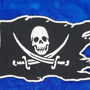 May include: A black pirate flag with a white skull and crossbones design. The flag is embroidered and has a frayed edge.