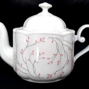 May include: White ceramic teapot with a lid and a curved handle. The teapot is decorated with a delicate pattern of green vines and small red leaves. The spout is long and curved.