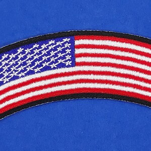 May include: A curved, embroidered patch featuring the American flag in red, white, and blue. The flag has a black border.