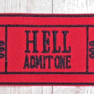 May include: Red fabric ticket with black stitching that reads "HELL ADMIT ONE" and "666" on either side.